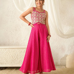Woman wearing a pink and white patterned top with a long pink skirt against a white curtain background.