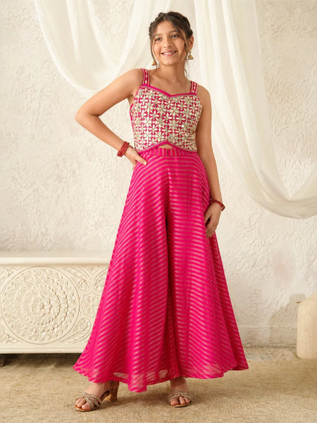 Woman wearing a pink and white patterned top with a long pink skirt against a white curtain background.
