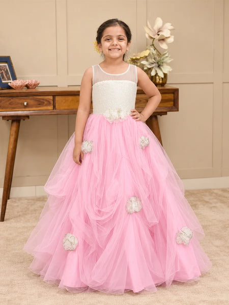 A young girl wearing a sleeveless white and pink flower girl dress with a beaded bodice, sheer neckline, and a pink tulle skirt with white fabric flowers.