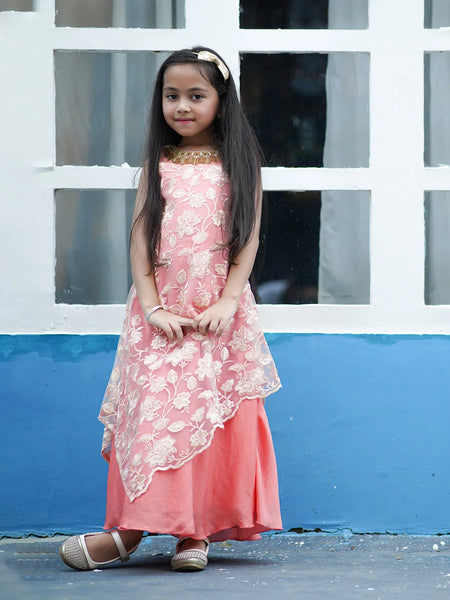 Young girl in a pink dress standing in front of a white and blue wall.