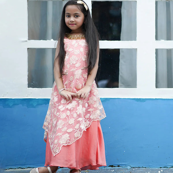 Young girl in a pink dress standing in front of a white and blue wall.