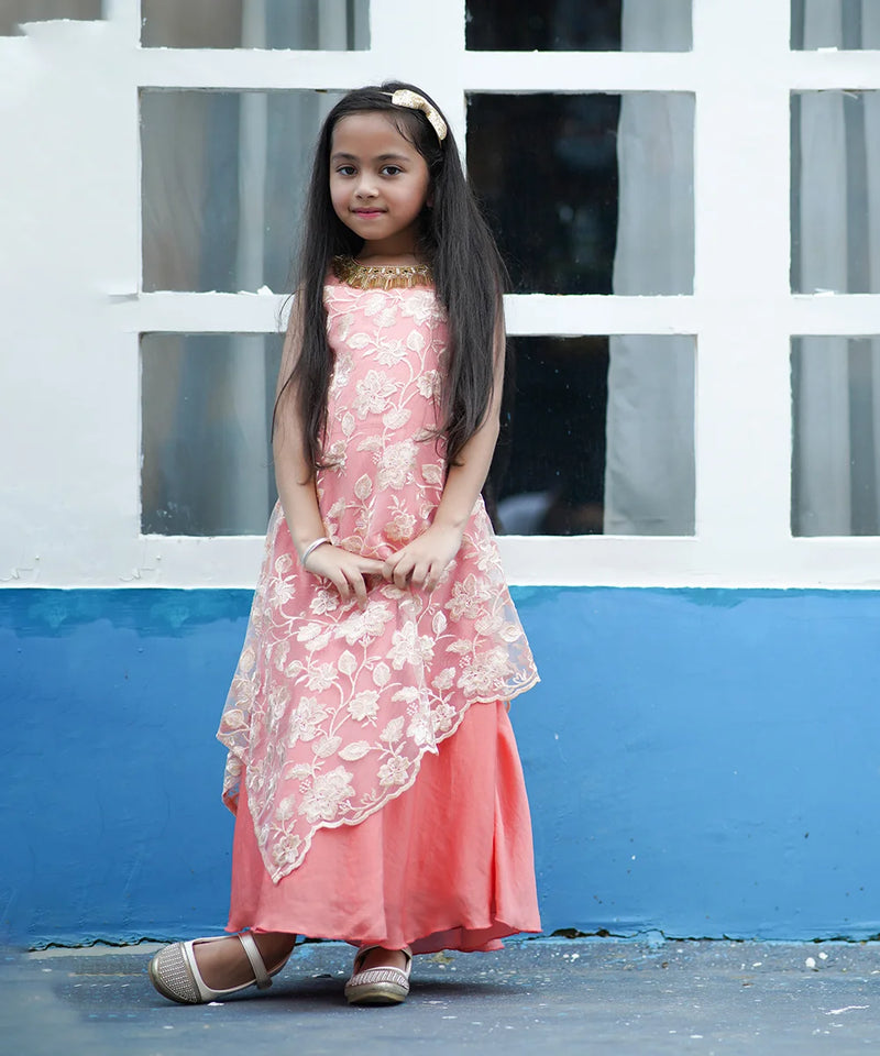 Young girl in a pink dress standing in front of a white and blue wall.