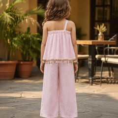 Young girl in a pink dress standing outdoors with plants and furniture in the background