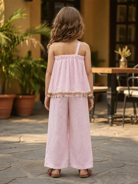 Young girl in a pink dress standing outdoors with plants and furniture in the background