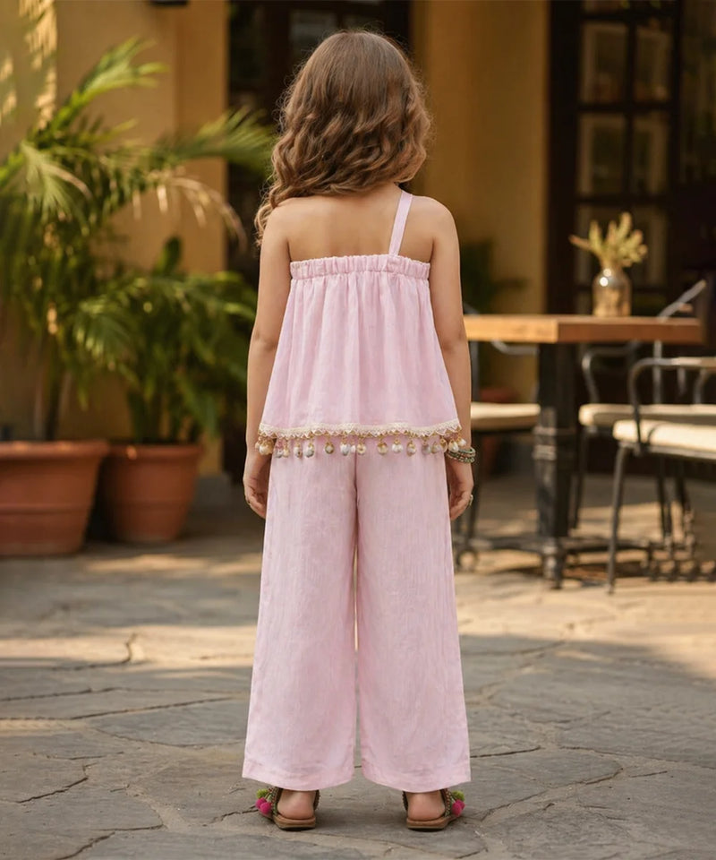 Young girl in a pink dress standing outdoors with plants and furniture in the background
