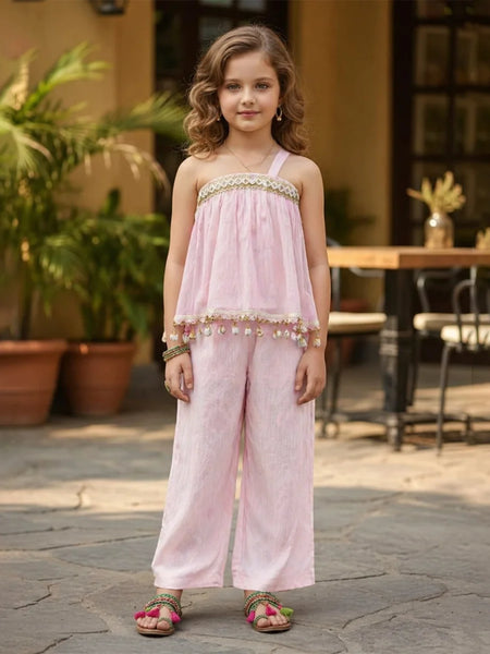 Young girl in a pink outfit standing outdoors with plants and furniture in the background