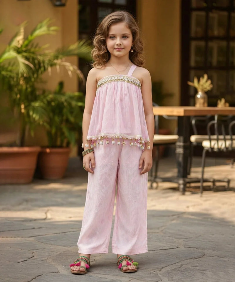 Young girl in a pink outfit standing outdoors with plants and furniture in the background