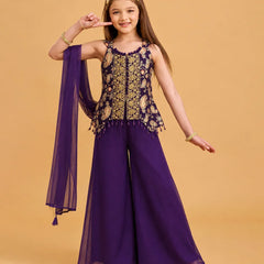 A young girl models a purple and gold traditional Indian outfit consisting of a sleeveless embroidered top with a matching sheer purple dupatta, set against a solid beige background.