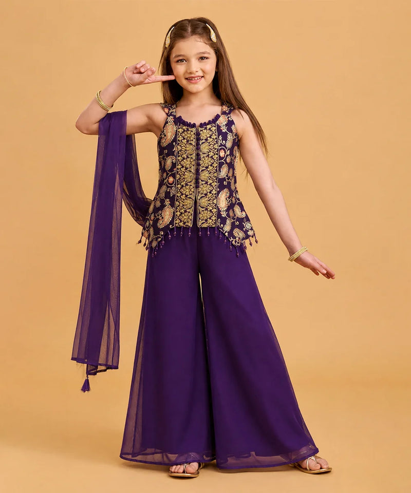 A young girl models a purple and gold traditional Indian outfit consisting of a sleeveless embroidered top with a matching sheer purple dupatta, set against a solid beige background.
