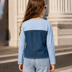 A child viewed from behind wearing a color-block denim jacket with light blue sleeves and upper back, and a darker blue denim back panel, paired with light-wash jeans in an outdoor setting with stone columns.