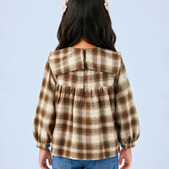 A child model shown from the back wearing a brown and beige plaid long-sleeve blouse with a wide collar and gathered back, paired with blue jeans against a light blue background.