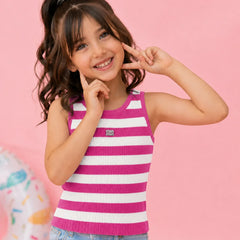 A young girl with dark brown hair in a high ponytail poses in a pink and white striped ribbed tank top and light blue jeans against a solid pink background.