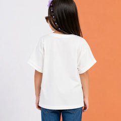 A child viewed from behind wearing an oversized white short-sleeve t-shirt and blue jeans, standing against a split white and orange background.