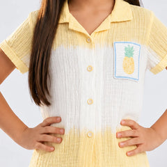 A child wearing a short-sleeve textured button-up shirt with a yellow-to-white ombré color-block design and a pineapple patch on the chest, photographed against a light gray studio background.