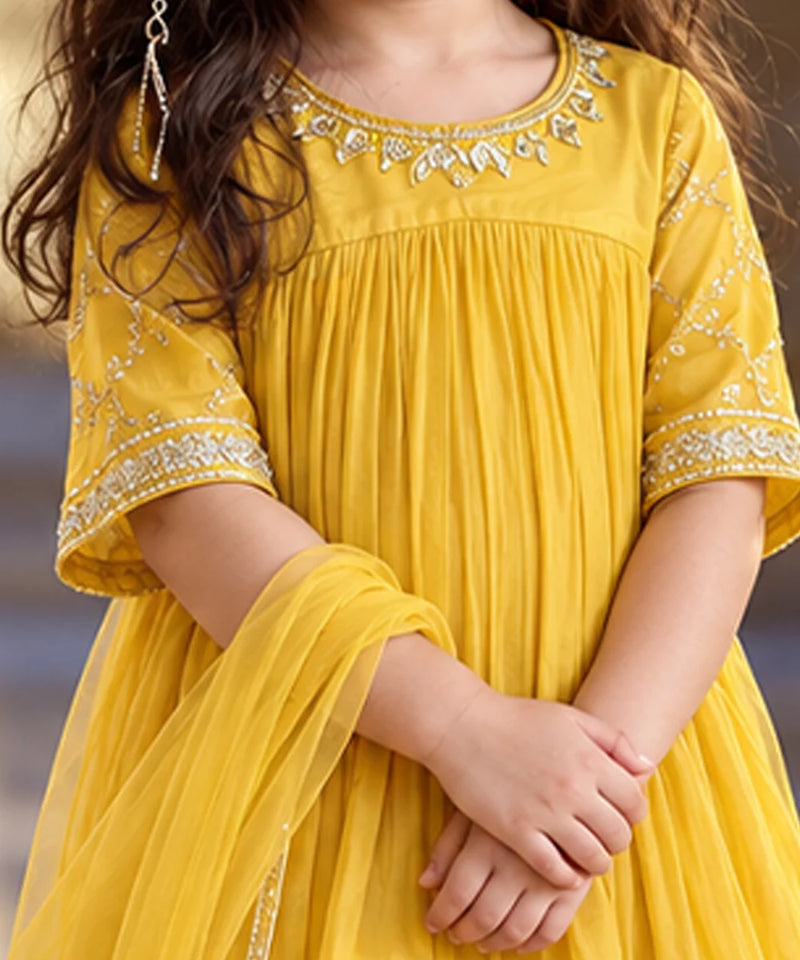 A close-up of a child wearing a bright yellow traditional dress with silver embroidered details around the neckline and sleeve cuffs, paired with a matching sheer dupatta.