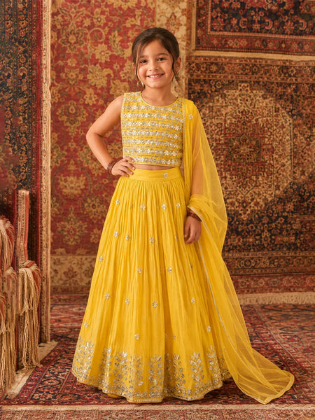 Young girl in a yellow traditional outfit standing on a patterned rug