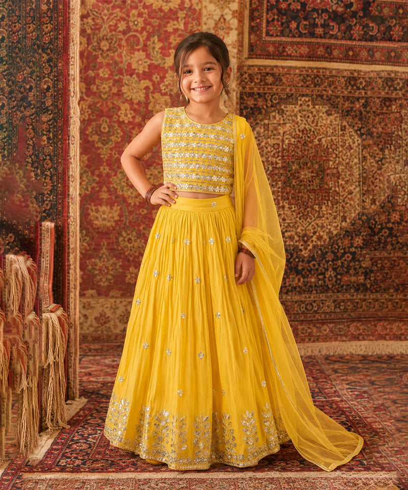 Young girl in a yellow traditional outfit standing on a patterned rug