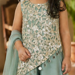 A child wearing a sleeveless mint green and beige embroidered traditional outfit with intricate lace embroidery, white floral appliques, and dangling tassel details, paired with a matching sheer dupatta.