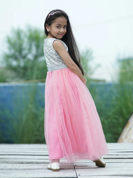 Young girl in a pink and silver dress standing on a wooden deck with greenery in the background