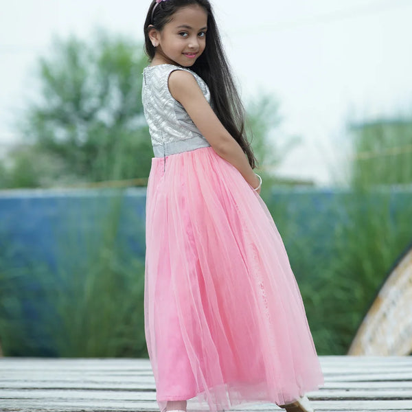 Young girl in a pink and silver dress standing on a wooden deck with greenery in the background