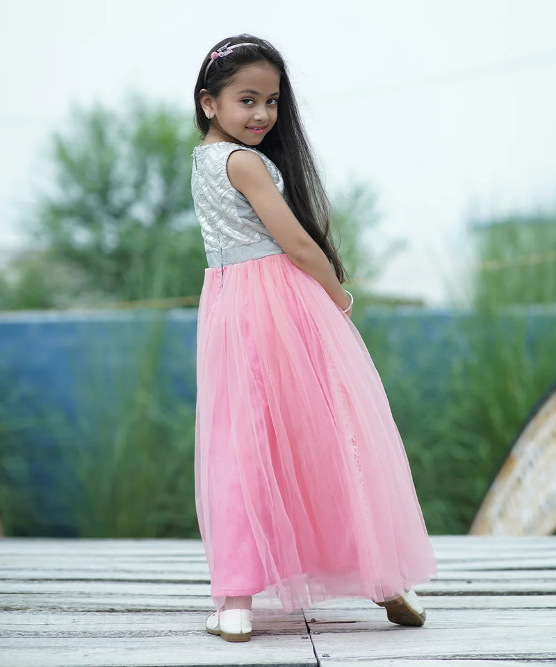 Young girl in a pink and silver dress standing on a wooden deck with greenery in the background