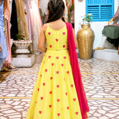 Young girl in a yellow dress with red heart patterns and a red dupatta in a store setting.