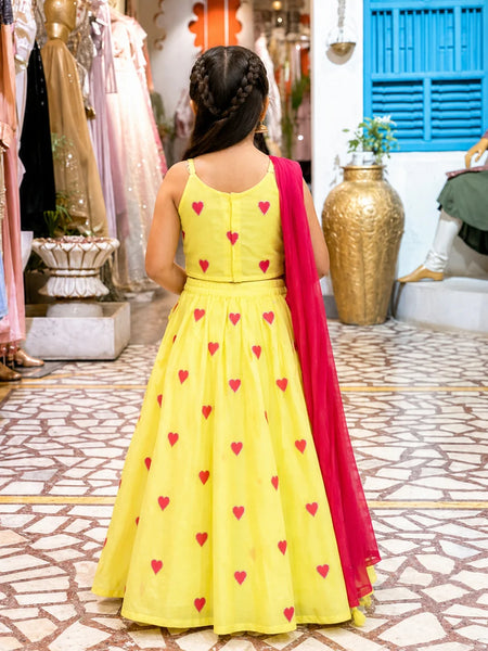 Young girl in a yellow dress with red heart patterns and a red dupatta in a store setting.