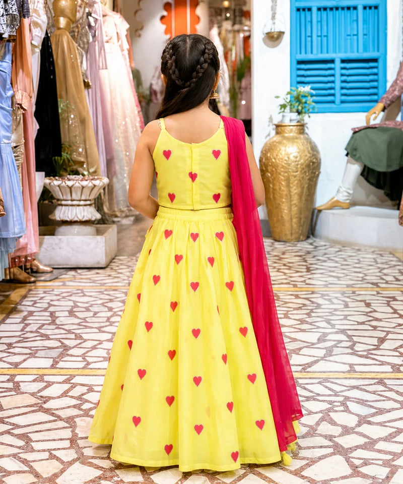 Young girl in a yellow dress with red heart patterns and a red dupatta in a store setting.