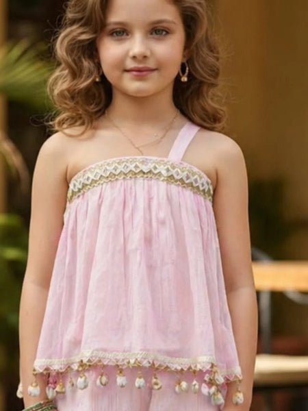 Young girl wearing a pink dress with gold accents outdoors.