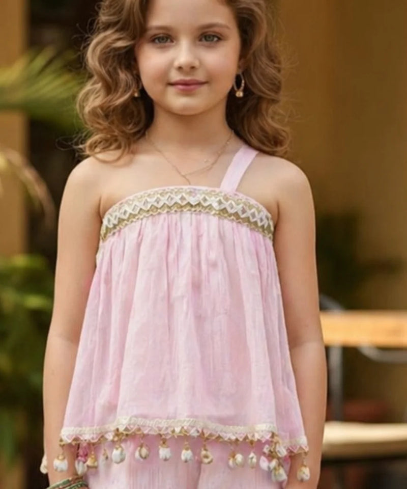 Young girl wearing a pink dress with gold accents outdoors.