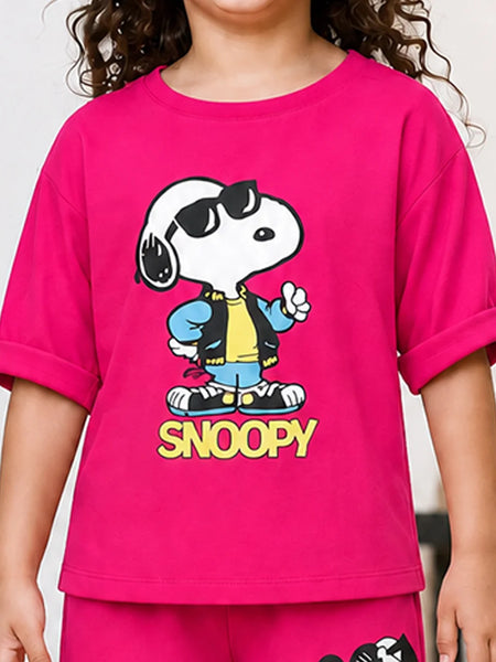 A child wearing a bright pink short-sleeve T-shirt with a large Snoopy graphic on the front. The graphic shows Snoopy wearing black sunglasses, a blue jacket, a yellow shirt, and blue jeans, with the word 'SNOOPY' printed below in yellow.