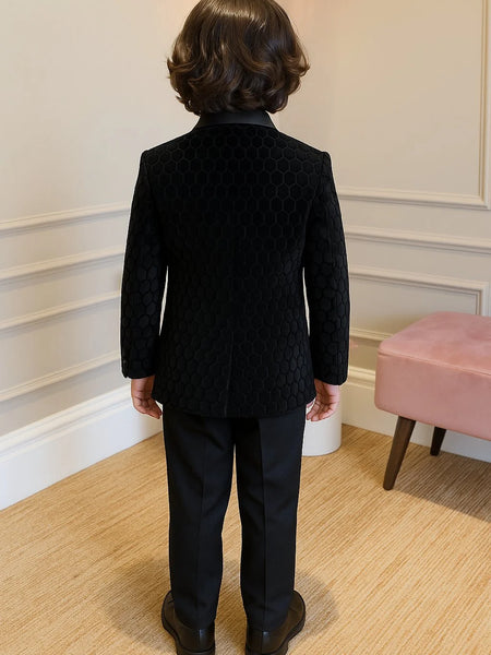 Person wearing a black textured jacket and pants standing in a room with a pink stool and white walls.