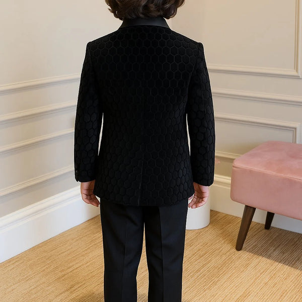 Person wearing a black textured jacket and pants standing in a room with a pink stool and white walls.
