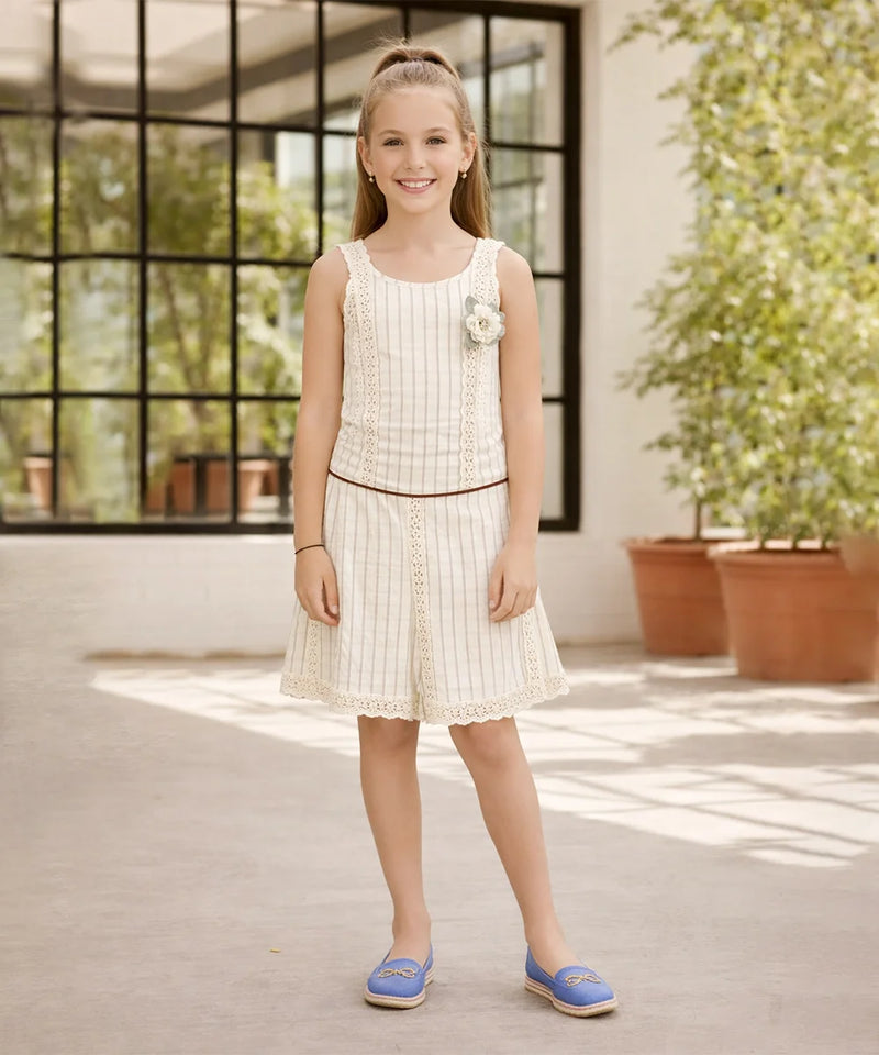 Young girl in a white dress standing in a sunlit room with large windows and plants.