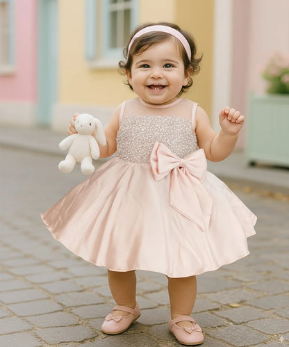 Child in a sparkly dress with a large bow holding a stuffed toy outdoors.