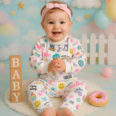 Baby in colorful pajamas with various patterns and text, sitting on a soft surface with a playful background.