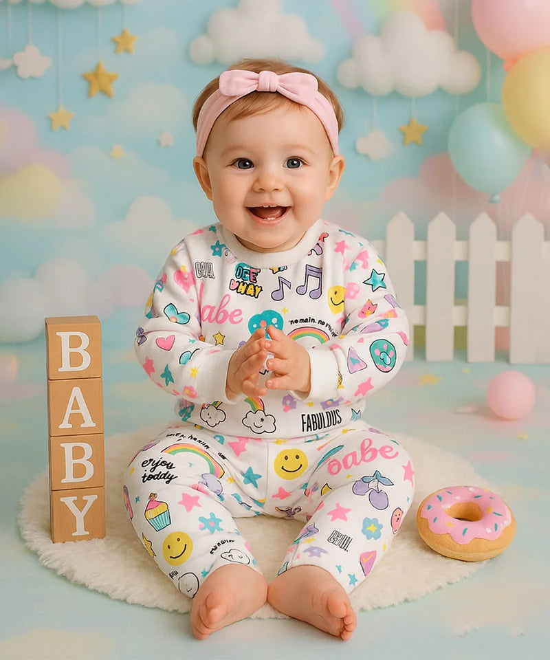 Baby in colorful pajamas with various patterns and text, sitting on a soft surface with a playful background.