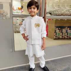 Child wearing a white kurta pyjama outfit with a gold emblem, standing in front of a store entrance.
