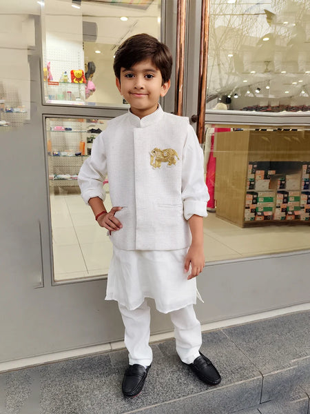 Child wearing a white kurta pyjama outfit with a gold emblem, standing in front of a store entrance.