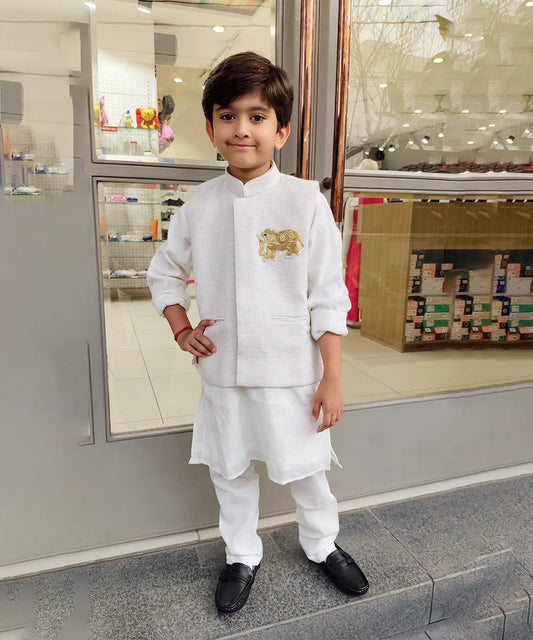 Child wearing a white kurta pyjama outfit with a gold emblem, standing in front of a store entrance.