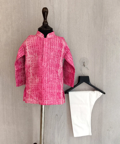 Pink patterned shirt on a mannequin and white pants on a hanger against a gray background