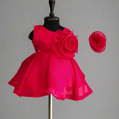 A red colored kids' party frock displayed on a mannequin, featuring a back zip closure, floral detailing on the waist, and paired with a matching hair accessory.