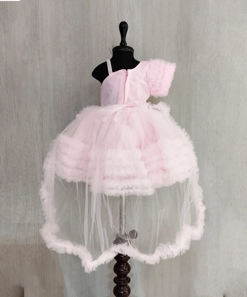 A beige knee-length party frock for girls, featuring a floral and time print, a round neck, sleeveless design, and a neon pink colored bow with an attached belt on the front.