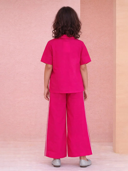 Person wearing a bright pink outfit with wide-leg pants against a pink and beige wall.