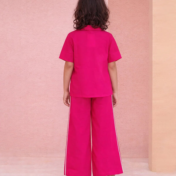 Person wearing a bright pink outfit with wide-leg pants against a pink and beige wall.