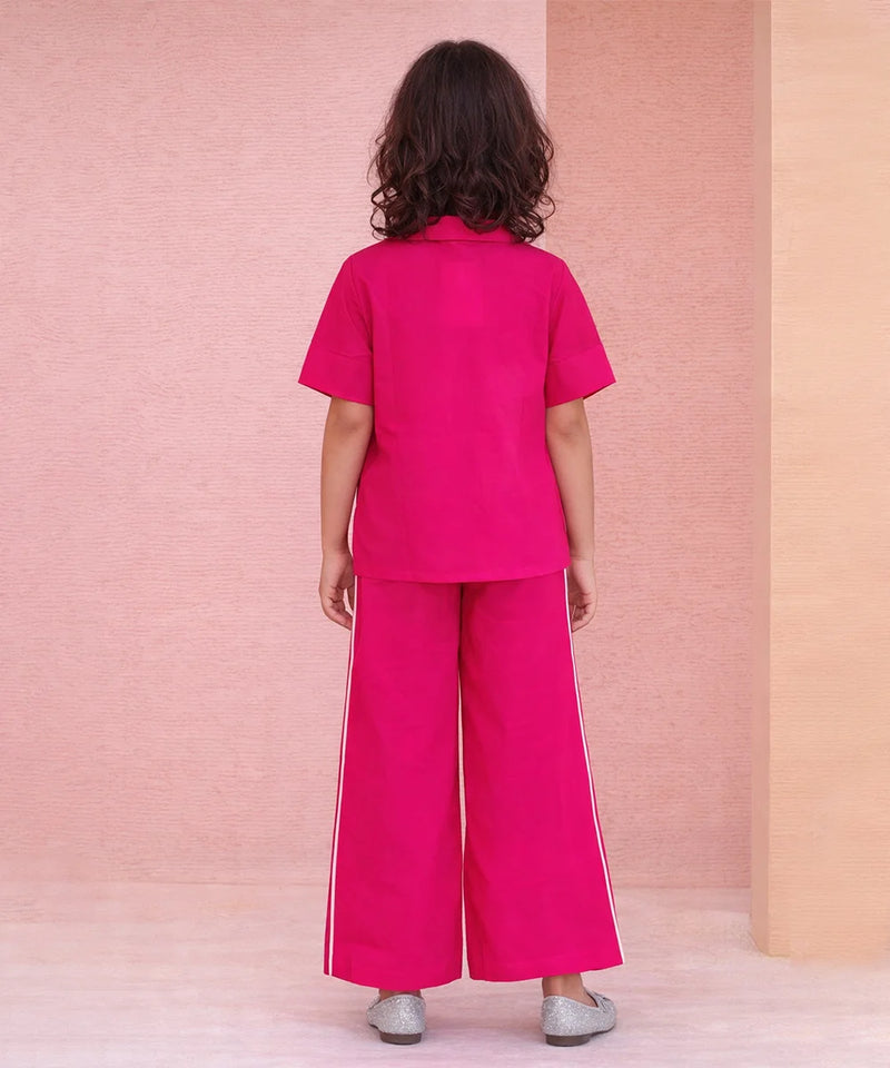 Person wearing a bright pink outfit with wide-leg pants against a pink and beige wall.