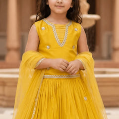Young girl in a yellow traditional outfit with intricate designs, standing outdoors.