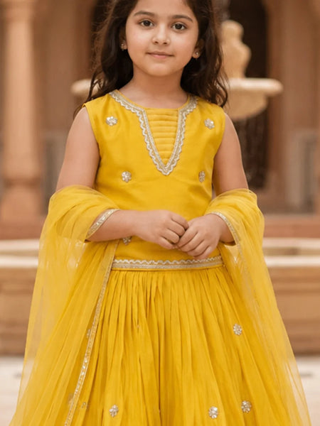 Young girl in a yellow traditional outfit with intricate designs, standing outdoors.