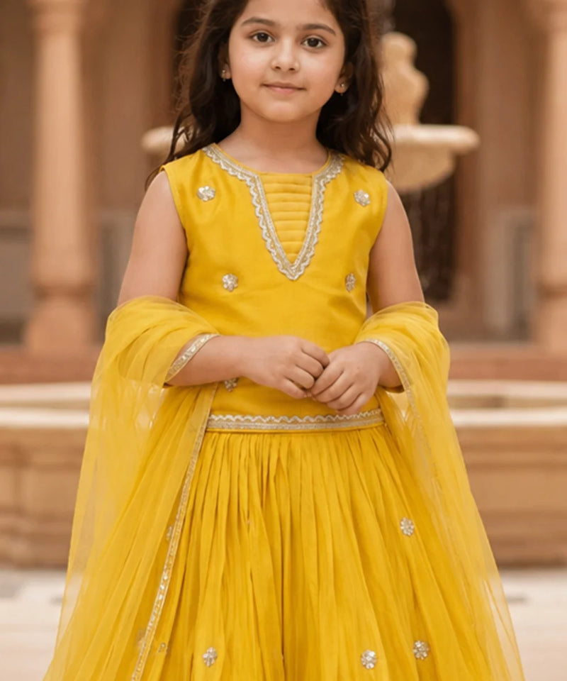 Young girl in a yellow traditional outfit with intricate designs, standing outdoors.