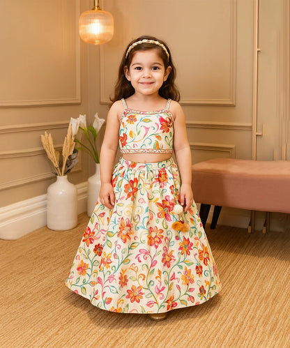 Young girl in a floral dress standing in a room with beige walls and a vase with flowers.